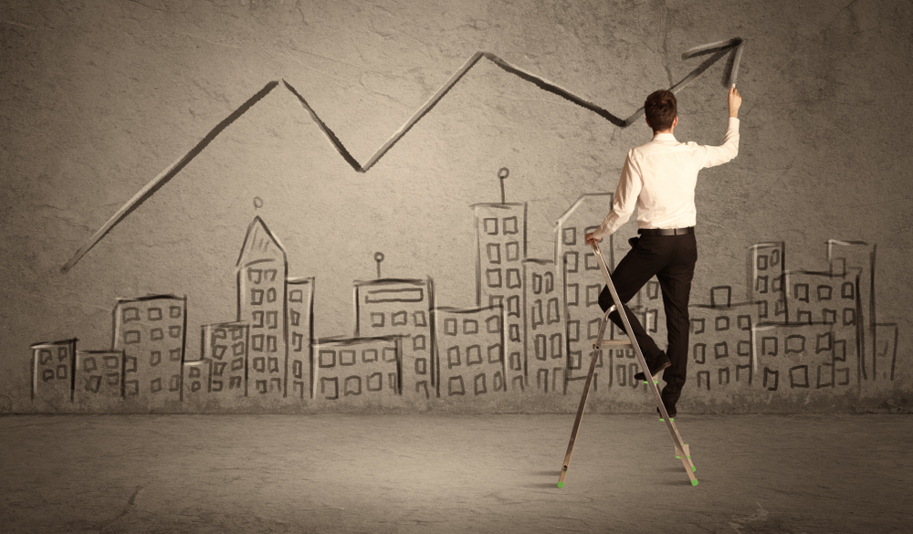 A man in elegant suit standing on a small ladder and drawing a line on brown wall background with buildings