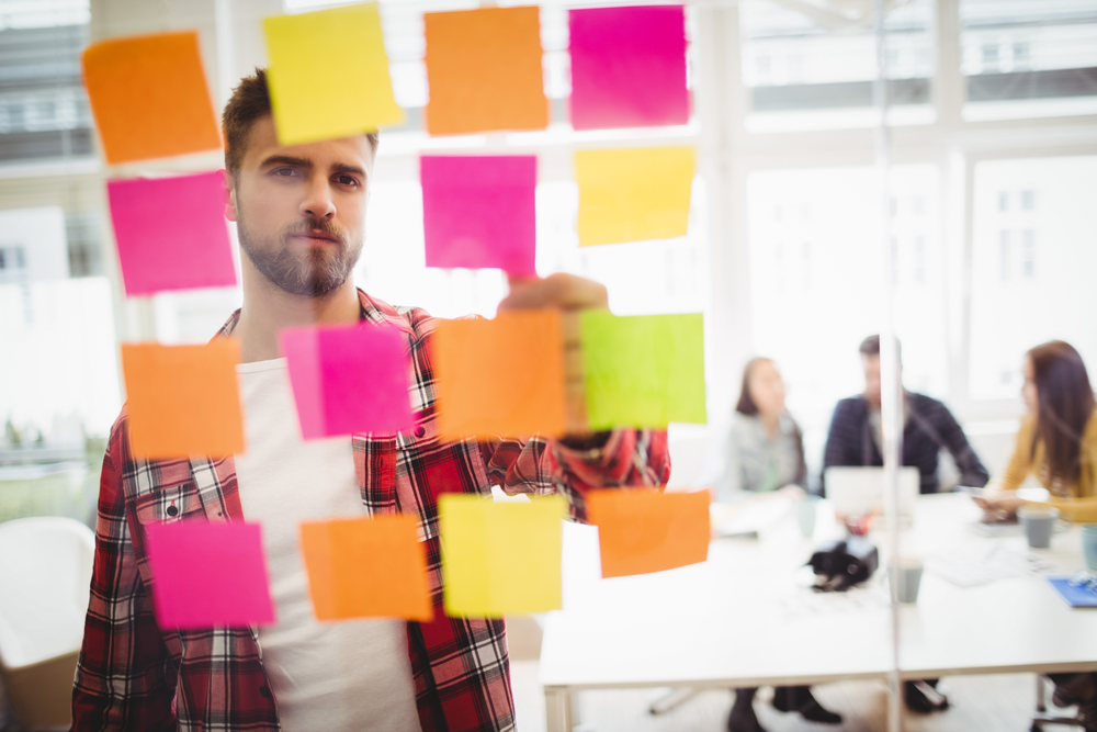 Photo editor looking at multi colored sticky notes on glass in meeting room at creative office Photo editor looking at multi colored sticky notes on glass in meeting room at creative office