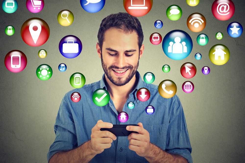 communication technology mobile phone high tech concept. Happy man using texting on smartphone social media application icons flying out of cellphone isolated grey wall background. 4g data plan communication technology mobile phone high tech concept. Happy man using texting on smartphone social media application icons flying out of cellphone isolated grey wall background. 4g data plan